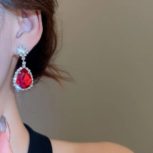 Detailed close-up of luxurious drop earrings with pear-cut red stone and sparkling diamonds