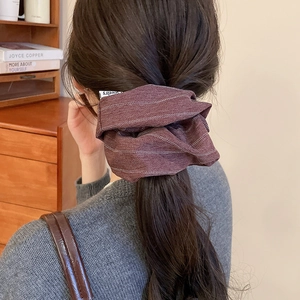 Detail of oversized dark brown herringbone fabric scrunchie worn on a low ponytail