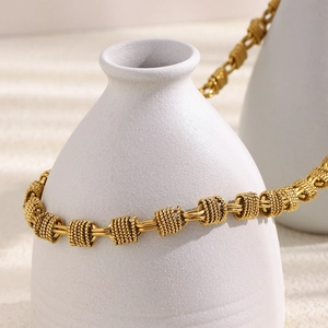 Detailed view of an 18K gold plated multi-layer coil necklace on a white vase