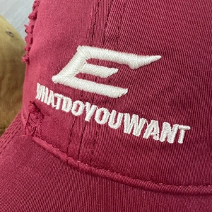 Detail of embroidered letters on distressed burgundy cotton twill baseball cap with rips