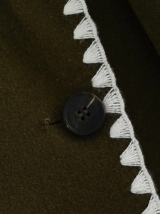 Detail of dark green wool coat with black button and white triangle fringe lace edge