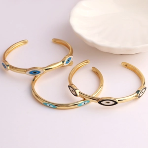 Detailed close-up of three gold-plated C-shaped evil eye bangles in blue and black enamel