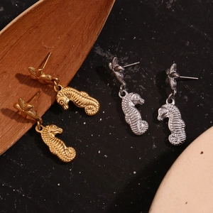 Detail of seahorse pendant earrings in gold and silver finish on textured dark background