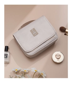 Closed beige hanging travel toiletry bag with brown TRAVEL label and elegant props