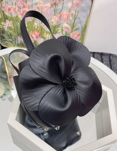 Detailed close-up of a black leather tote featuring a large layered 3D floral decoration