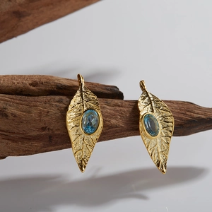 Detail view of gold leaf earrings with blue oval gemstones resting on natural wood