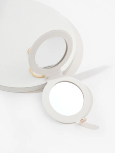 Detail of round white PU leather pocket mirror with gold metal ring on geometric props