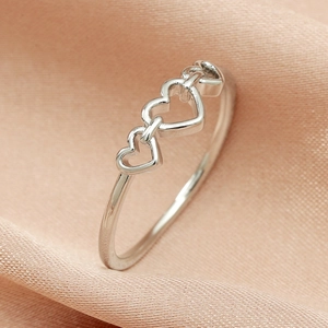 Close-up of triple interconnected hollow heart-shaped silver metal rings on silk