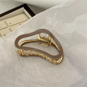 Detail of metal shark hair claw clip in latte brown and gold finish on white paper