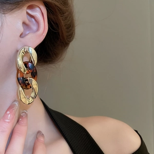Macro detail of tortoiseshell resin and gold link chain earrings worn by a model