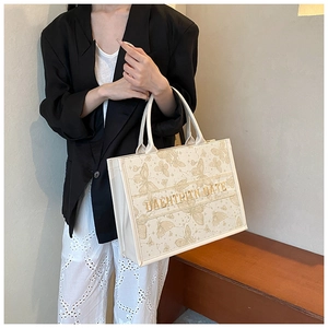 Detail of off-white tote bag with gold butterfly prints and embroidered stripe text