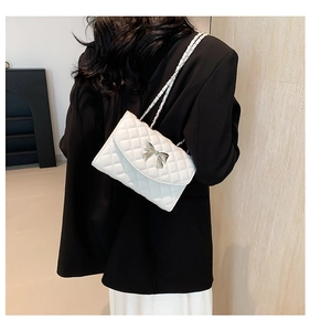 Détail d'un sac à main matelassé blanc avec nœud argenté sur une veste noire chic