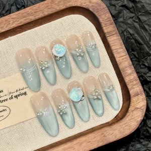 Detailed view of handmade almond press-on nails with blue cat-eye shimmer and floral rhinestones