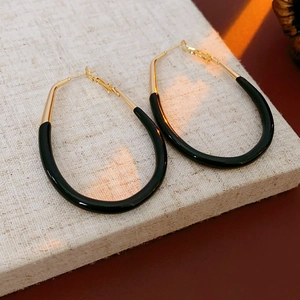 Macro detail of U-shaped gold earrings with premium black enamel finish on beige surface