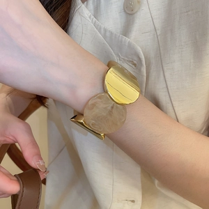 Détail d'un bracelet gourmette en métal doré et résine marbrée crème sur mannequin