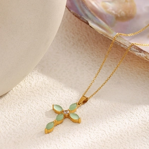 Détail du collier croix en acier plaqué or 18K avec pierre verte sur plateau en céramique