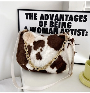 Close-up of plush cow print tote bag with gold chain strap and fluffy charm detail