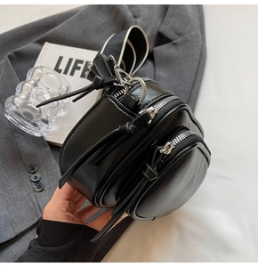 Detail of black round crossbody bag with lychee texture and bicolor wide strap