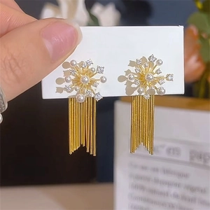 Detail view of gold tassel earrings with pearls and crystals on a white display card
