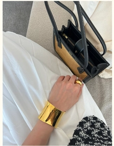 Macro shot of polished gold-plated wide cuff and chunky ring on hand with elegant dress
