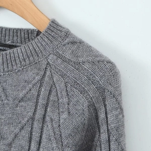 Detail of the crew neck and cable knit texture on a gray fashion sweater on a hanger