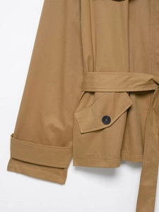 Detailed view of khaki trench coat featuring cuff straps, buttoned pocket and belt fabric