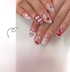 Dettaglio di unghie finte a mandorla con disegni di ciliegie rosse e fiocchi bianchi