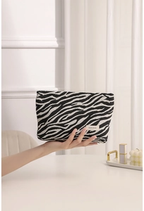 Close-up of zebra pattern fabric makeup bag held in hand featuring an H&R brand label