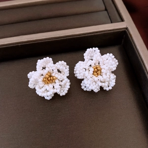 Close-up of handmade white and gold bead woven camellia flower earrings on a velvet tray