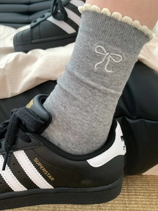 Detailansicht grauer Baumwollsocken mit weißen Rüschen und aufgestickter Schleife