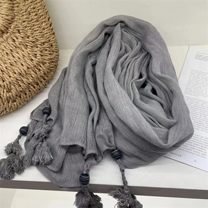 Gray voile headscarf with handmade tassel beads shown with a straw bag on a white table