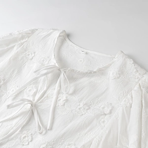 Close-up of white long sleeve top with detailed floral embroidery and tie neckline