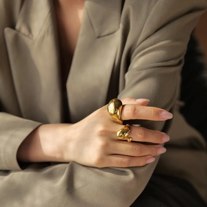 Detail shot of chunky 18K gold plated fluid design stainless steel rings on a model's hand