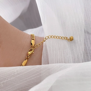 Detail of a gold Cuban link chain bracelet with extension and round pendant on soft fabric