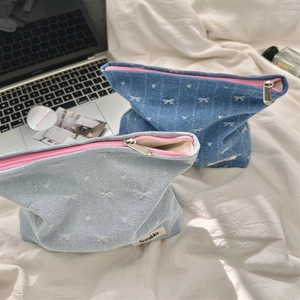 Close-up of denim cosmetic bags with embroidered white bows and pink zipper detail