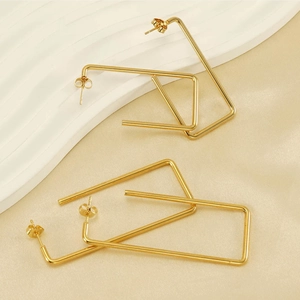 Macro shot of gold rectangle hoop earrings on beige textured and white rippled background