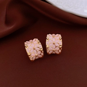 Detail of 18k gold plated earrings with pink enamel flower patterns on brown fabric