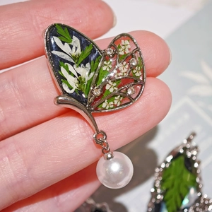 Vue macro d'une broche papillon avec de vraies fleurs séchées, résine et pendentif perle