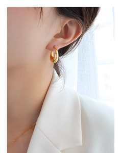 Gros plan d'une boucle d'oreille dorée en forme de C au style minimaliste français