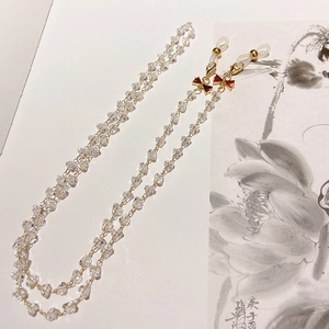 Detail of crystal glasses chain with red bows and gold lobster clasps on floral background