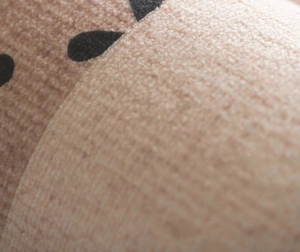 Macro detail of breathable skin-tone bandage featuring a black water droplet pattern
