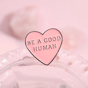 Detailed close-up of a pink heart-shaped enamel pin featuring Be A Good Human message