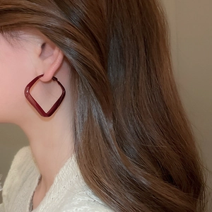Detail view of large dark red geometric square hoop earrings worn by a female model