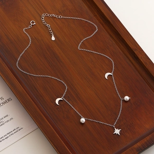 Close-up of s925 silver star and moon necklace with pearls on a wooden tray