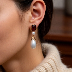 Close-up of vintage drop earrings with red gemstone and pearls on a model profile