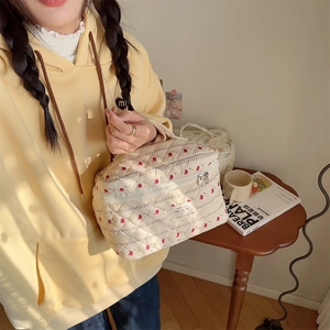 Gros plan d'une trousse à maquillage matelassée à fleurs avec poignée tenue à la main