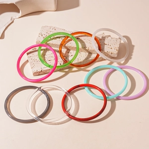 Colorful acrylic resin bangles in candy shades displayed on textured stone pedestals