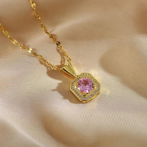 Detail of a square gold pendant necklace with a pink center stone on beige cloth