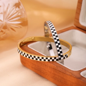Minimalist stainless steel checkerboard enamel bangles in gold and silver on a wooden box