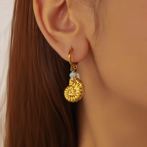 Gold hoop earrings with conch shell pendant and light blue beads on a female model